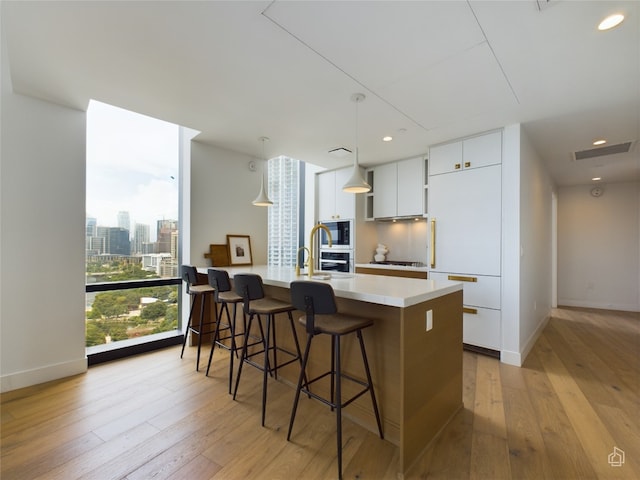 kitchen featuring hanging light fixtures, light hardwood / wood-style floors, an island with sink, and white cabinets