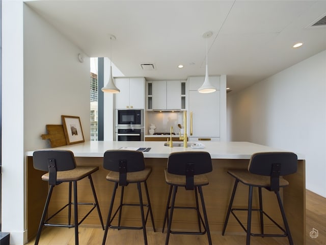 kitchen with built in microwave, a breakfast bar, hardwood / wood-style flooring, oven, and white cabinets