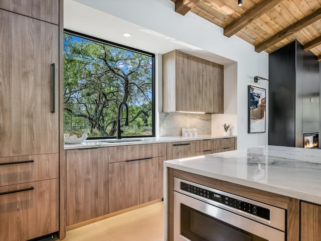 kitchen with stainless steel oven, backsplash, light stone counters, wooden ceiling, and lofted ceiling with beams