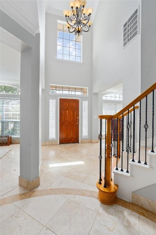 entrance foyer with an inviting chandelier, a towering ceiling, and ornamental molding