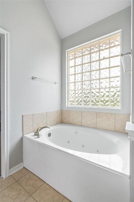 bathroom featuring vaulted ceiling, a healthy amount of sunlight, a bathing tub, and tile patterned flooring