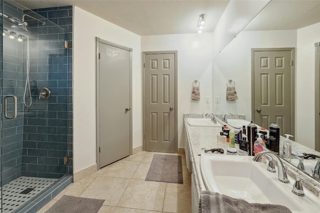 bathroom with a textured ceiling, tile patterned floors, walk in shower, and dual bowl vanity