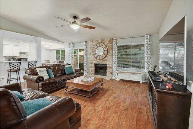 living room featuring ceiling fan, a fireplace, light hardwood / wood-style flooring, and vaulted ceiling