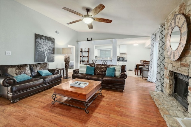 living room with light hardwood / wood-style flooring, a fireplace, ceiling fan, and vaulted ceiling