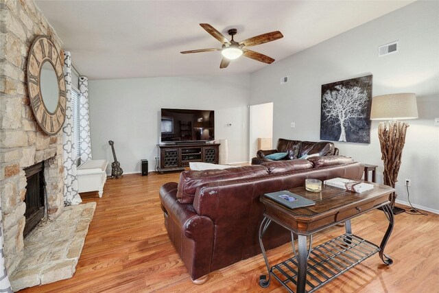 living room featuring a stone fireplace, ceiling fan, and light hardwood / wood-style floors