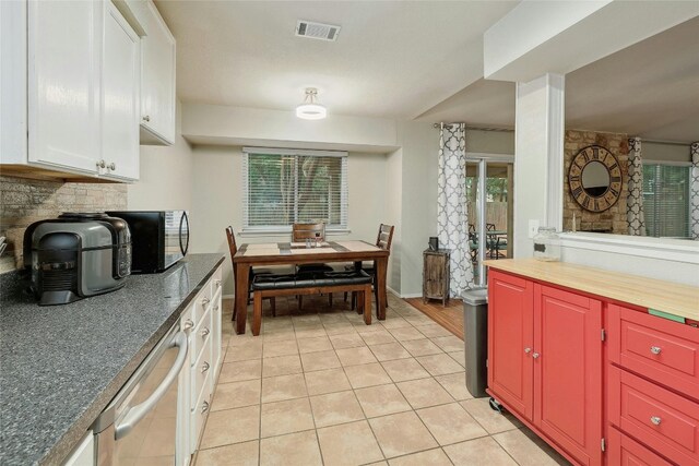 kitchen featuring white cabinets, stainless steel dishwasher, light tile patterned flooring, and plenty of natural light