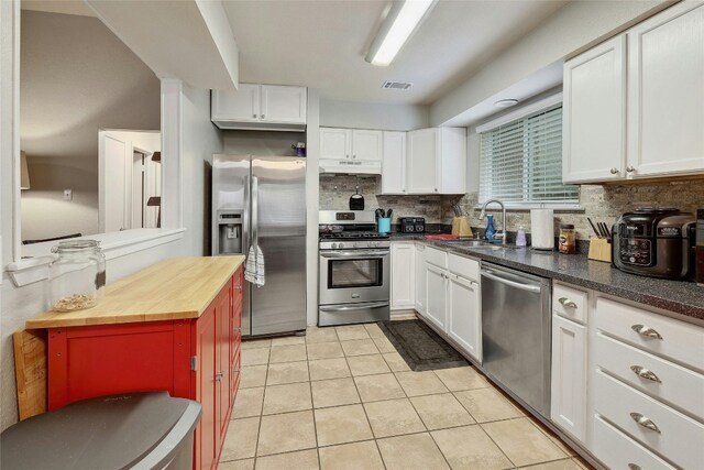 kitchen featuring light tile patterned flooring, backsplash, white cabinetry, and appliances with stainless steel finishes