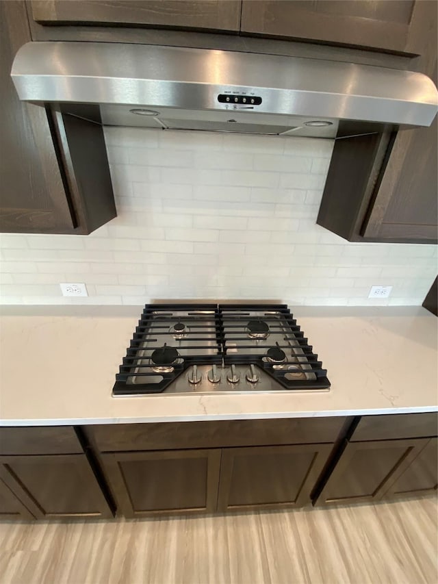 kitchen featuring range hood, stainless steel gas stovetop, backsplash, dark brown cabinets, and light wood-type flooring