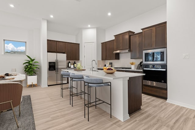 kitchen featuring a breakfast bar, sink, tasteful backsplash, a center island with sink, and appliances with stainless steel finishes