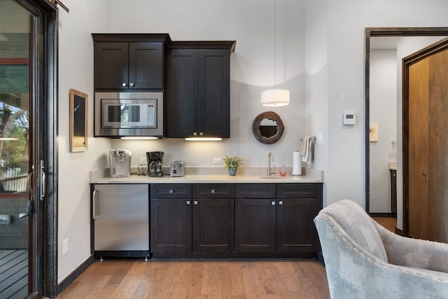 kitchen with stainless steel microwave, refrigerator, sink, hanging light fixtures, and light hardwood / wood-style floors