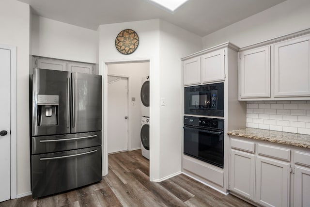 kitchen with tasteful backsplash, black appliances, hardwood / wood-style floors, and stacked washer / drying machine