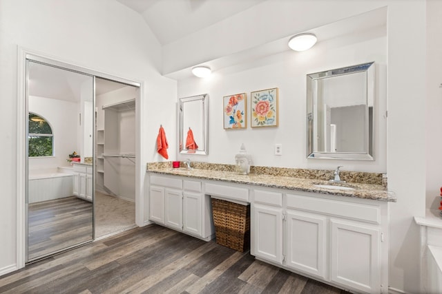 bathroom with double vanity, lofted ceiling, hardwood / wood-style floors, and a tub