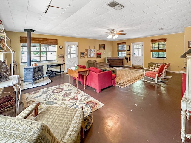 living room with concrete floors, a wood stove, and ceiling fan