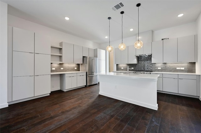 kitchen featuring sink, high end refrigerator, dark hardwood / wood-style floors, pendant lighting, and a kitchen island with sink