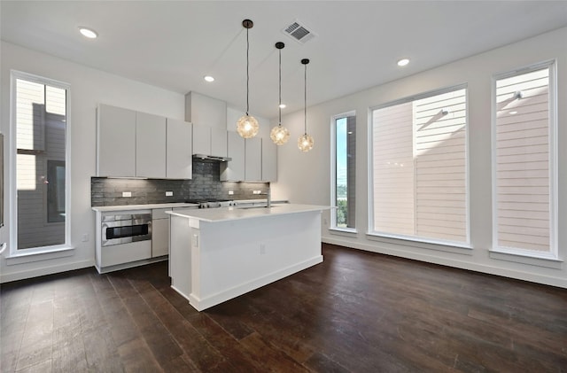 kitchen featuring sink, tasteful backsplash, decorative light fixtures, dark hardwood / wood-style flooring, and a kitchen island with sink