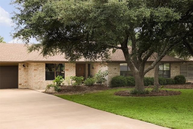 ranch-style home featuring a garage, concrete driveway, a shingled roof, and a front yard