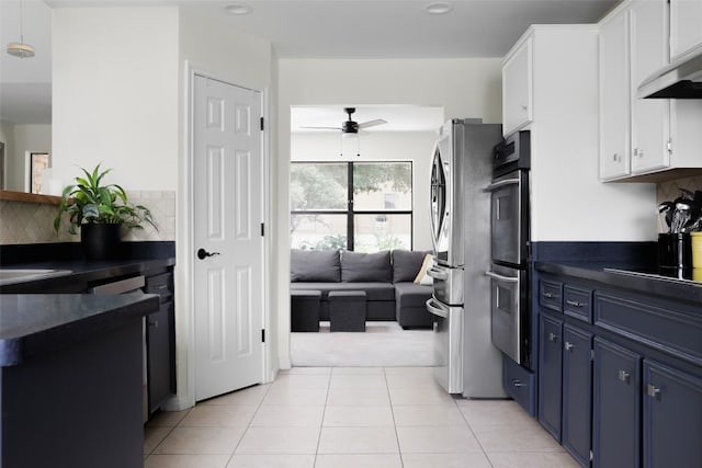 kitchen with dark countertops, blue cabinets, under cabinet range hood, double oven, and light tile patterned flooring