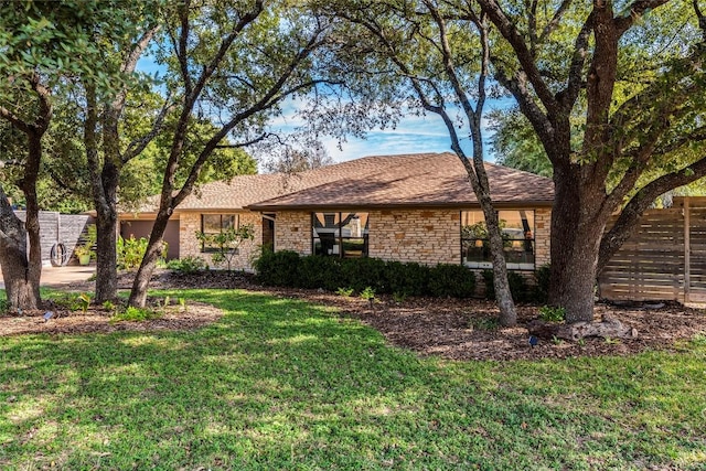 ranch-style house with a garage, stone siding, roof with shingles, and a front lawn