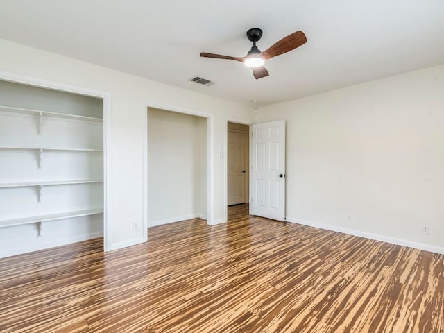 unfurnished bedroom featuring wood finished floors, two closets, visible vents, and baseboards