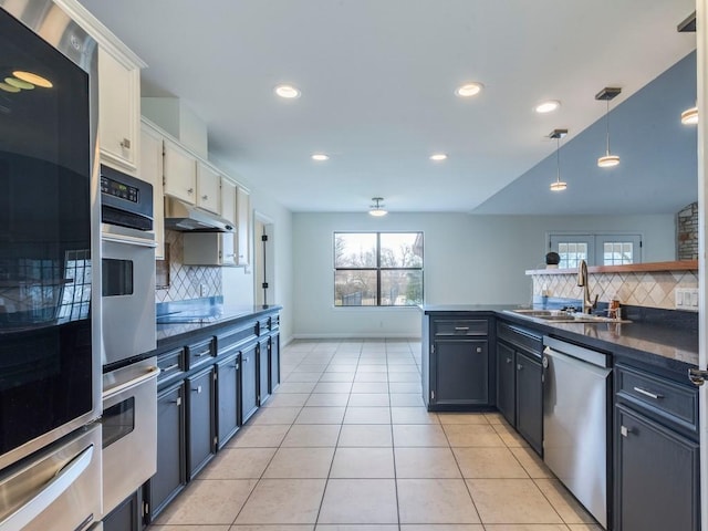 kitchen featuring a warming drawer, dark countertops, stainless steel dishwasher, a sink, and under cabinet range hood