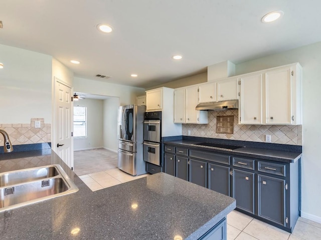 kitchen with appliances with stainless steel finishes, a sink, under cabinet range hood, white cabinetry, and backsplash