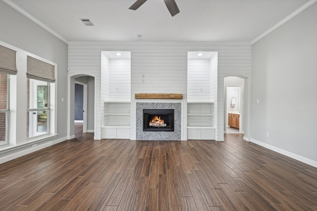 unfurnished living room featuring crown molding, dark wood-type flooring, built in shelves, and ceiling fan