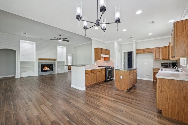 kitchen with dark hardwood / wood-style flooring, ceiling fan with notable chandelier, ornamental molding, a center island, and stove