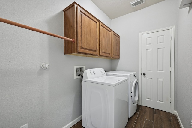 clothes washing area featuring washing machine and clothes dryer, dark hardwood / wood-style flooring, and cabinets