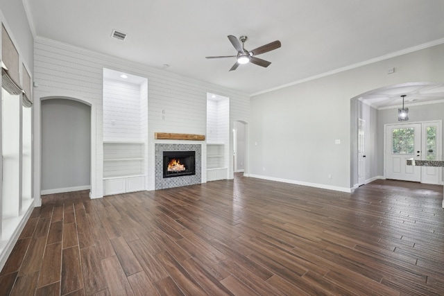 unfurnished living room featuring dark wood-type flooring, built in shelves, ceiling fan, and ornamental molding