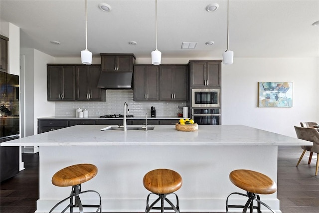 kitchen featuring sink, decorative light fixtures, stainless steel appliances, and a center island with sink