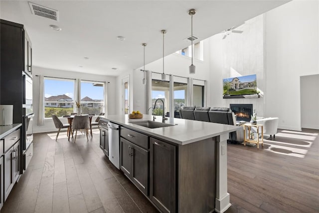 kitchen with sink, a tile fireplace, appliances with stainless steel finishes, hanging light fixtures, and a center island with sink