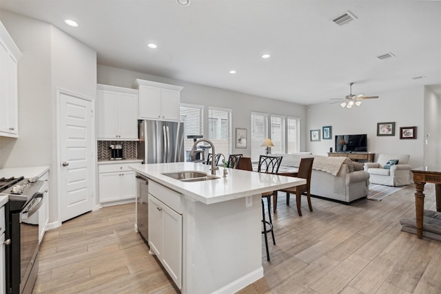 kitchen with sink, a kitchen island with sink, white cabinetry, appliances with stainless steel finishes, and light hardwood / wood-style floors