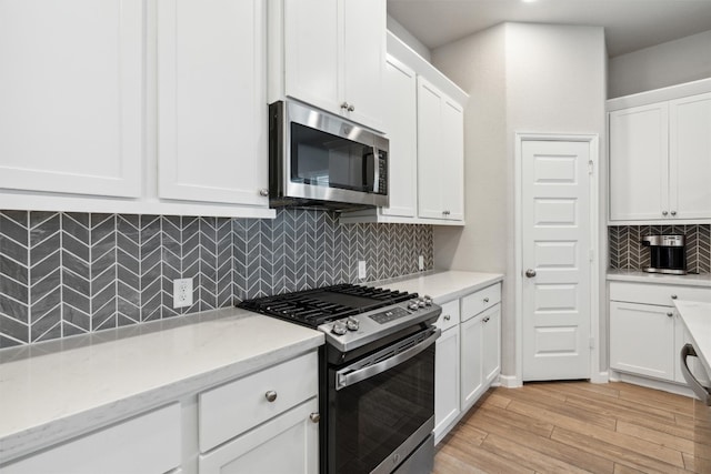 kitchen with light stone counters, tasteful backsplash, white cabinetry, appliances with stainless steel finishes, and light wood-type flooring