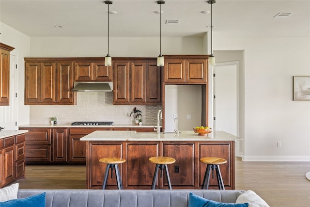 kitchen with a kitchen bar, a center island with sink, hardwood / wood-style floors, pendant lighting, and gas stovetop