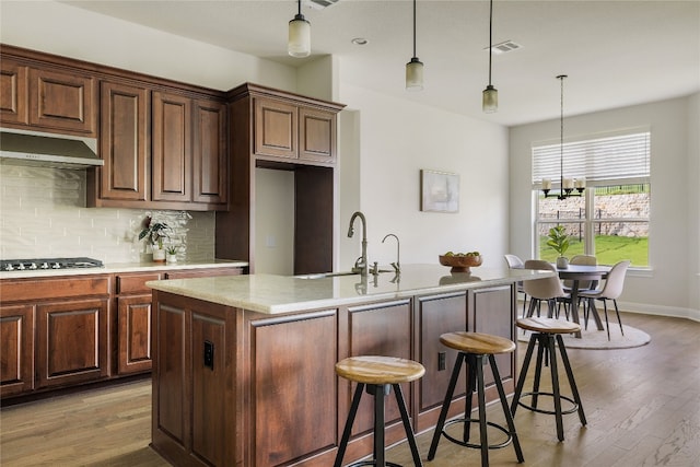 kitchen with decorative backsplash, stainless steel gas stovetop, light wood-type flooring, sink, and a center island with sink