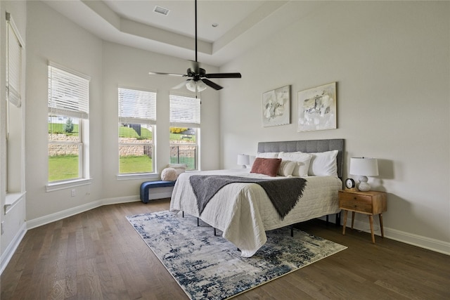 bedroom with ceiling fan, dark wood-type flooring, and a tray ceiling