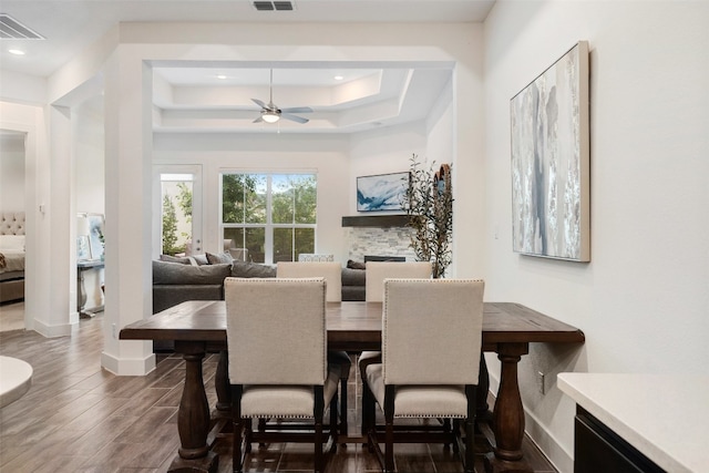 dining space featuring a fireplace, dark hardwood / wood-style flooring, a raised ceiling, and ceiling fan