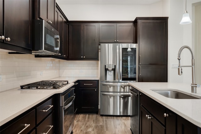 kitchen with sink, dark brown cabinetry, decorative light fixtures, wood-type flooring, and stainless steel appliances