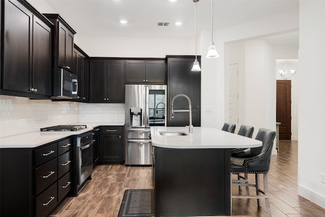 kitchen featuring a breakfast bar, stainless steel appliances, dark wood-type flooring, pendant lighting, and a center island with sink