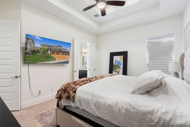 bedroom featuring a raised ceiling, ensuite bath, ceiling fan, and light carpet