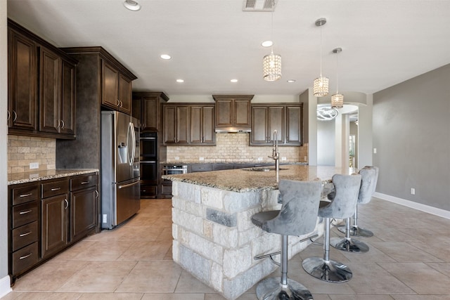 kitchen with decorative backsplash, hanging light fixtures, sink, stainless steel fridge with ice dispenser, and light stone countertops