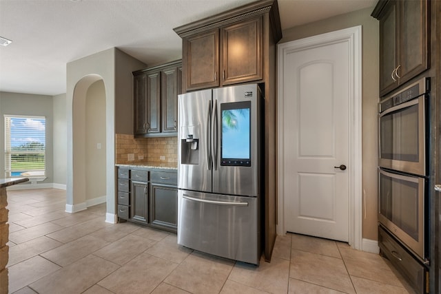 kitchen with stainless steel appliances, dark brown cabinetry, light tile patterned flooring, and decorative backsplash