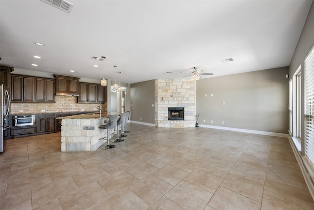 kitchen featuring a kitchen island with sink, backsplash, decorative light fixtures, appliances with stainless steel finishes, and light stone counters