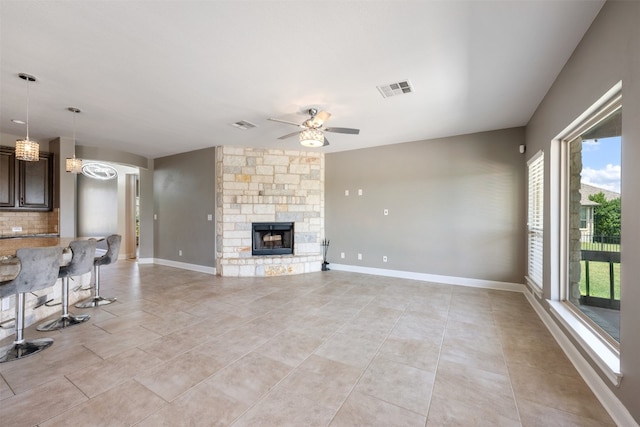 unfurnished living room with ceiling fan, a fireplace, light tile patterned floors, and plenty of natural light