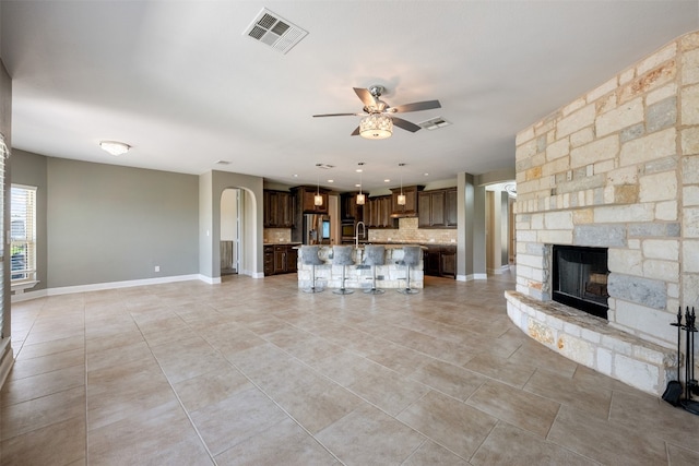 unfurnished living room with a stone fireplace, light tile patterned floors, and ceiling fan