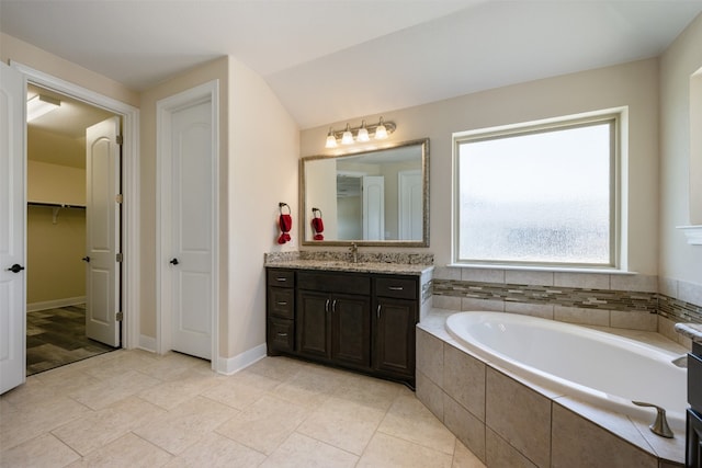 bathroom featuring vanity, a relaxing tiled tub, and vaulted ceiling