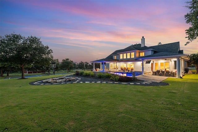 back house at dusk featuring a lawn