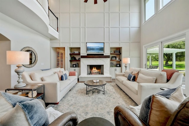 living room with built in features, a high ceiling, a fireplace, and ceiling fan