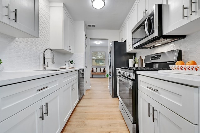 kitchen featuring light hardwood / wood-style flooring, backsplash, appliances with stainless steel finishes, and white cabinetry