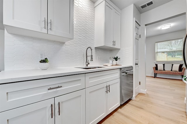 kitchen with light hardwood / wood-style floors, tasteful backsplash, stainless steel dishwasher, sink, and white cabinetry